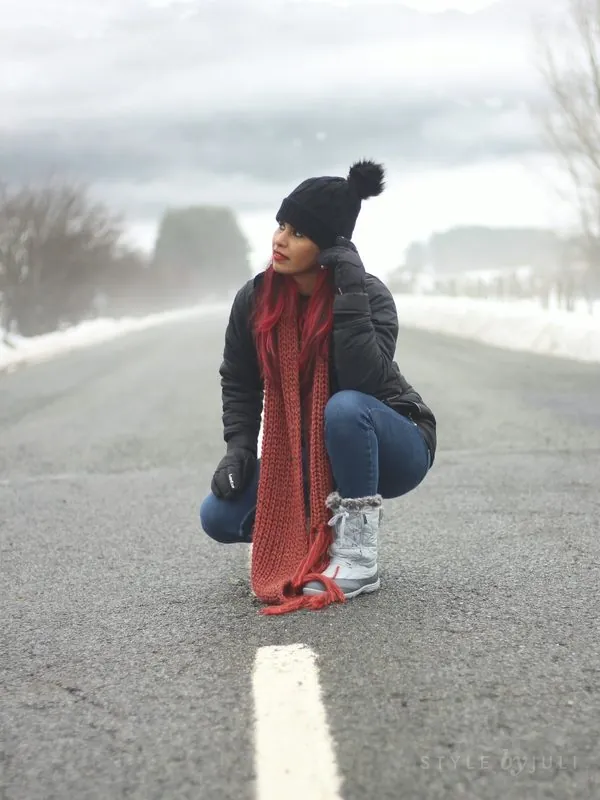 Juli en una carretera nevada con melena roja, gorro negro y bufanda roja